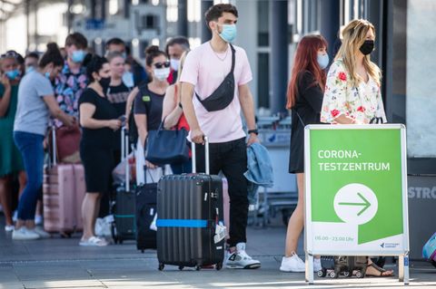 Reiserückkehrer aus Spanien stehen mit Mundschutz vor dem Corona-Testzentrum am Flughafen Stuttgart an