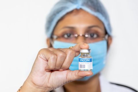 Indischer Arzt in chirurgischer Maske hält eine Impfstoffflasche in die Kamera.