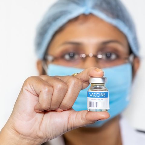 Indischer Arzt in chirurgischer Maske hält eine Impfstoffflasche in die Kamera.