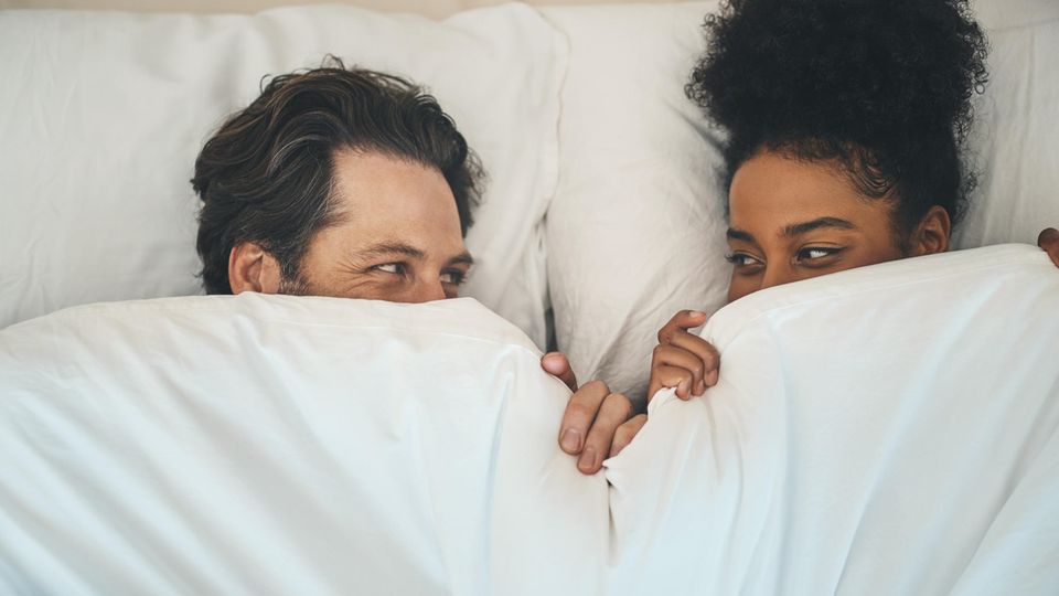 Penisring: Ein Pärchen liegt im Bett und schaut sich in die Augen.