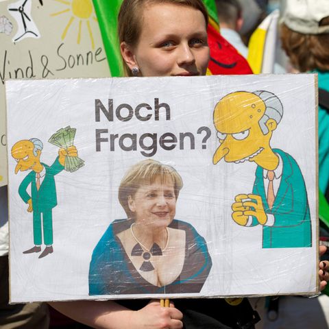 Eine Demonstrantin hält in Gronau ein Transparent gegen Atomkraft mit Merkel und Mister Burns drauf in der Hand.
