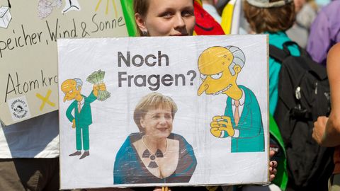 Eine Demonstrantin hält in Gronau ein Transparent gegen Atomkraft mit Merkel und Mister Burns drauf in der Hand.