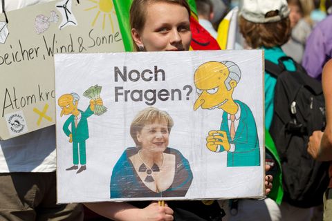 Eine Demonstrantin hält in Gronau ein Transparent gegen Atomkraft mit Merkel und Mister Burns drauf in der Hand.