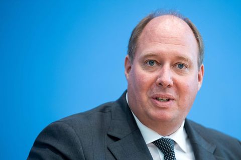 Ein beleibter Mann mit Halbglatze sitzt in Anzug und Krawatte vor einem blauen Hintergrund