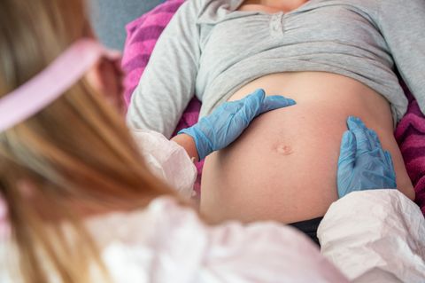 Eine Hebamme trägt Schutzausrüstung und untersucht eine schwangere Frau