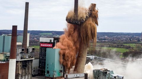 Ein gemauerter Schornstein sackt nach einer Sprengung in drei Teilen und einer Staubwolke zusammen