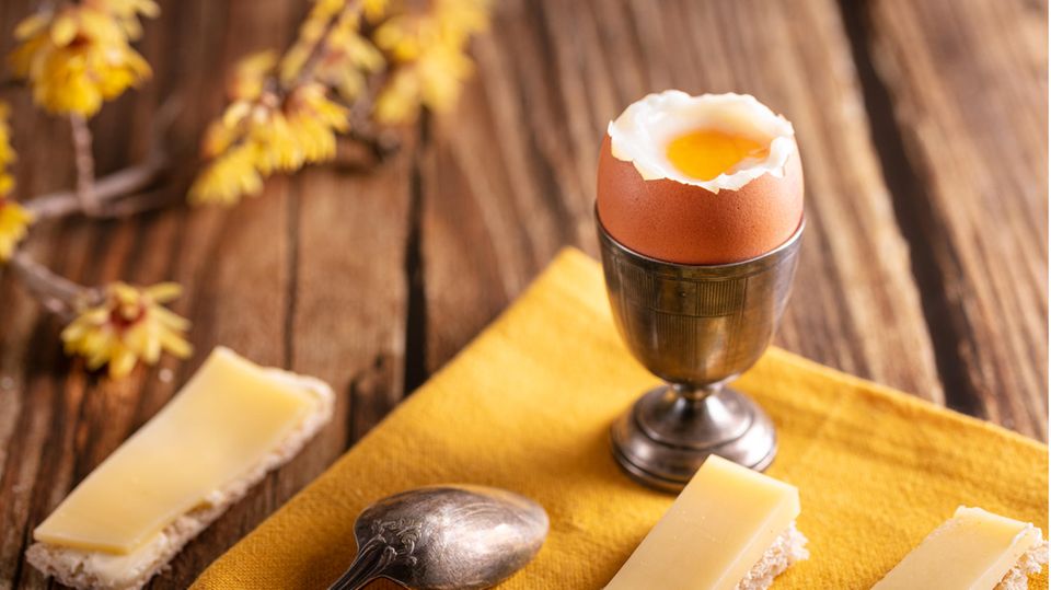 Frühstückstisch mit Käsebroten und einem weich gekochten Ei im Becher
