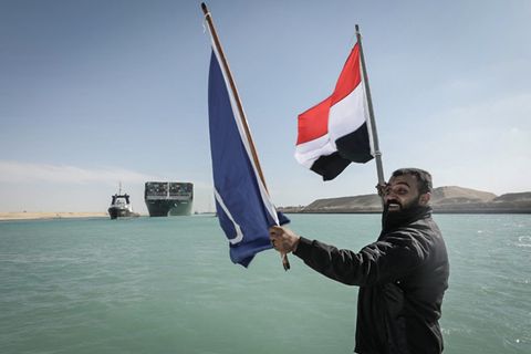 Ein Arbeiter schwenkt eine Flagge Ägyptens, im Hintergrund das Containerschiff "Ever Given" 