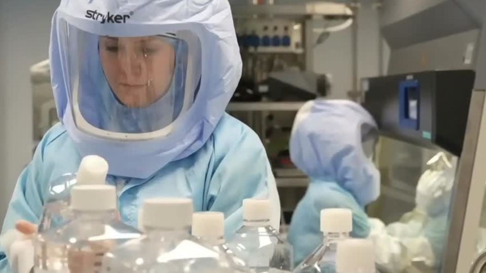 Eine Frau mit hellblauem Schutzanzug inklusiive luftdichter Haube arbeitet in einem Labor