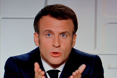 Frankreichs Präsident Macron sitzt in einem TV-Studio vor weißem Hintergrund und zeigt mit beiden Händen auf die TV-Zuschauer