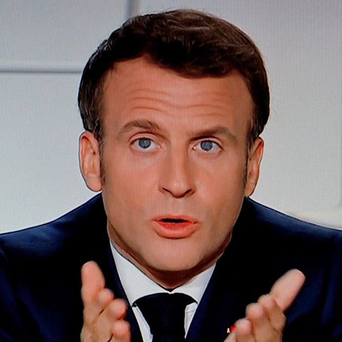 Frankreichs Präsident Macron sitzt in einem TV-Studio vor weißem Hintergrund und zeigt mit beiden Händen auf die TV-Zuschauer