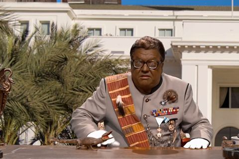 Satiriker Helmut Schleich sitzt als afrikanischer Despot mit schwarz angemaltem Gesicht am Schreibtisch