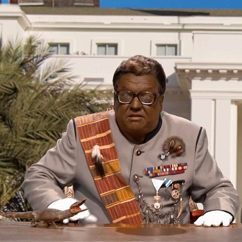 Satiriker Helmut Schleich sitzt als afrikanischer Despot mit schwarz angemaltem Gesicht am Schreibtisch