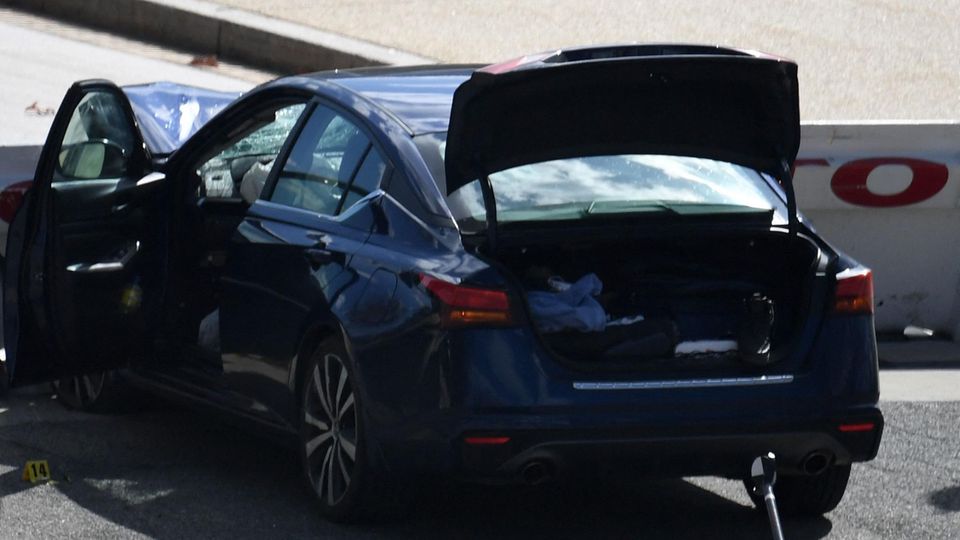 Ein dunkelblauer BMW steht mit offenem Kofferraum, Fahrertür und Motorhaube zerstört an einer Beton-Barriere