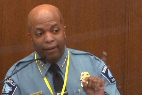 Ein Schwarzer mit Glatze und in Polizie-Uniform gestikuliert hinter einer Glasscheibe in einem Gerichtssaal
