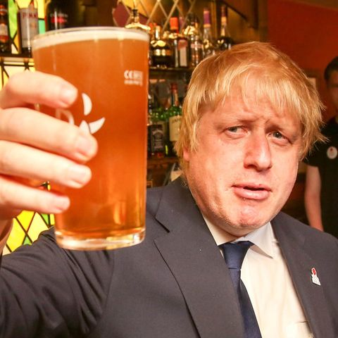 Ein blonder, propperer Mann im Anzug erhebt ein Pint-Glas mit Bier, während er in einem englischen Pub steht