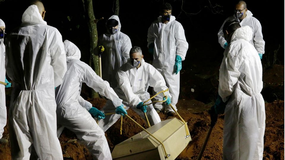 Brasilien Corona Totengräber Sieben Männer in weißen Schutzanzügen senken einen hellen Holzsarg mit einem Corona-Toten in ein Grab