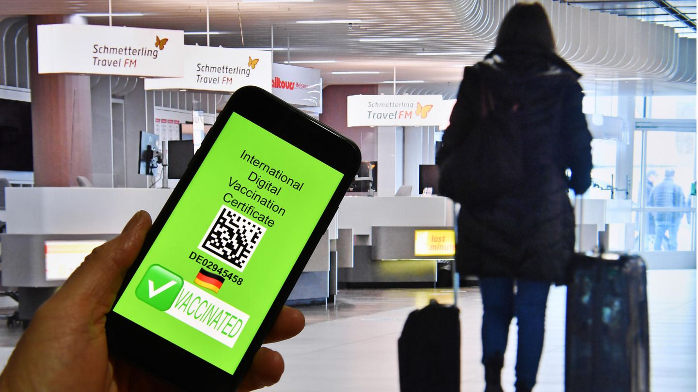 Eine Hand hält ein Handy, dahinter ist eine Szene im Flughafen zu sehen