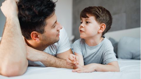 Vater und Sohn liegen auf dem Bett, der Junge redet