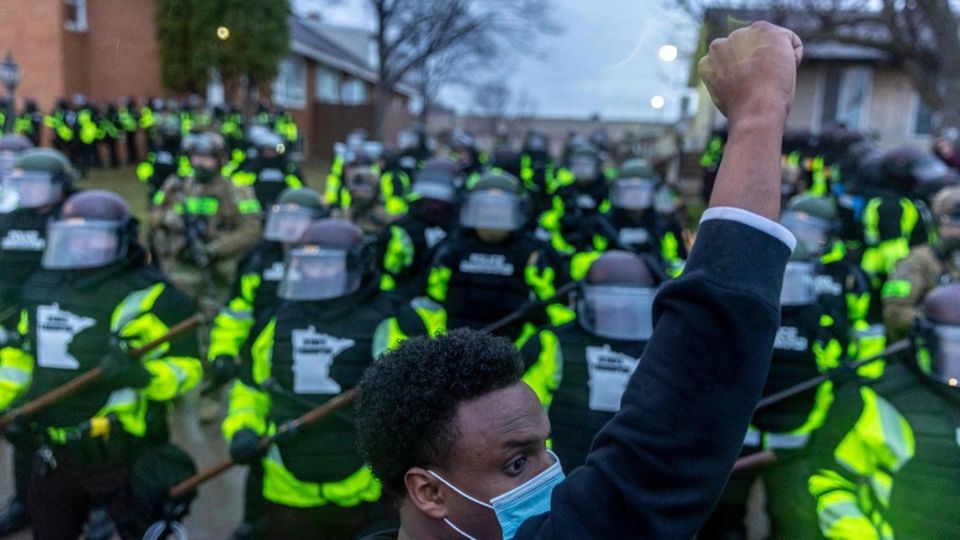 Ein junger schwarzer Mann mit Gesichtsmaske protestiert, dahinter sind Polizisten zu sehen