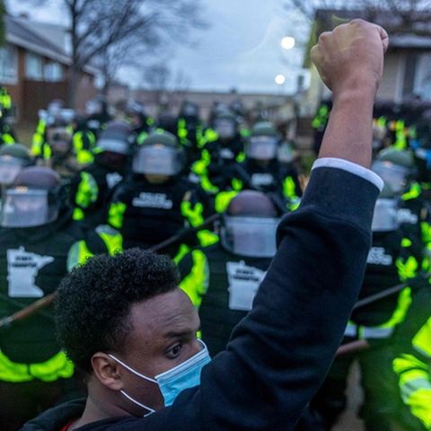 Ein junger schwarzer Mann mit Gesichtsmaske protestiert, dahinter sind Polizisten zu sehen