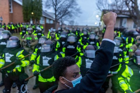 Ein junger schwarzer Mann mit Gesichtsmaske protestiert, dahinter sind Polizisten zu sehen