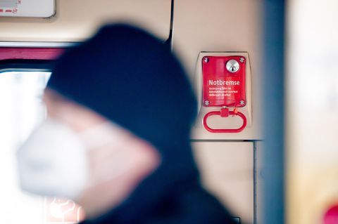 Ein Fahrgast mit Mund-Nasen-Schutz steht in einer Berliner S-Bahn vor einer Notbremse