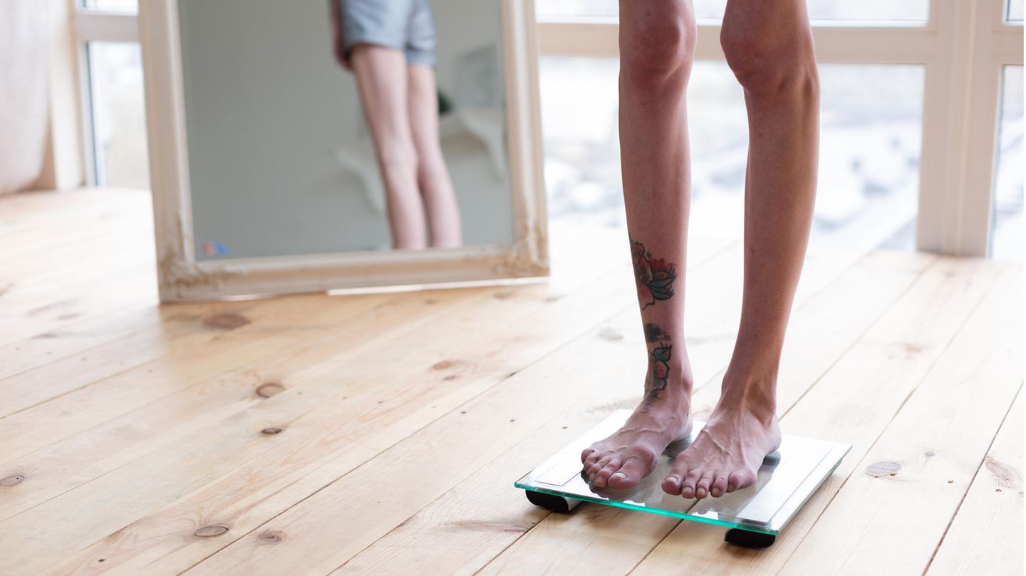 Eine dünne Frau steht auf einer Waage. Ihre Beine und Knie sind sehr dünn