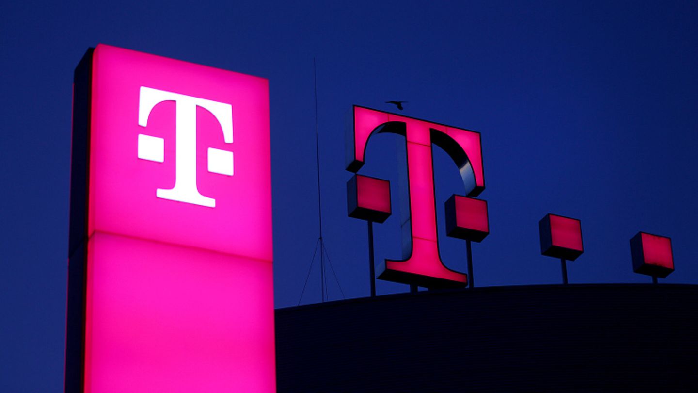 Das Logo der Deutschen Telekom leuchtet vor einem dunklen Himmel auf dem Dach der Unternehmenszentrale