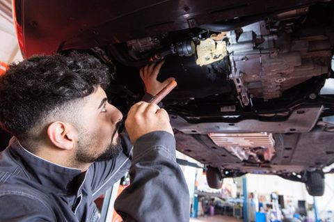 KfZ-Mechatroniker untersucht Schäden an Unterseite eines Wagens.