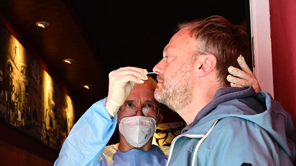 Ein Mann in medizinischer Schutzkleidung steht in der Tür einer Bar und steckt einem anderen Mann ein Wattestäbchen in die Nase