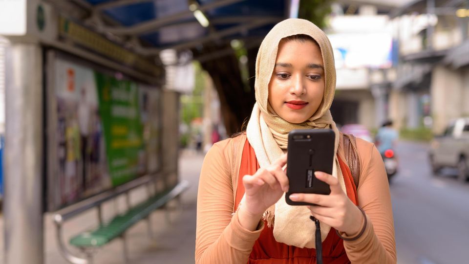 Eine Muslima trägt ein Kopftuch und blickt auf ihr Handy