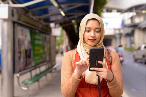 Eine Muslima trägt ein Kopftuch und blickt auf ihr Handy