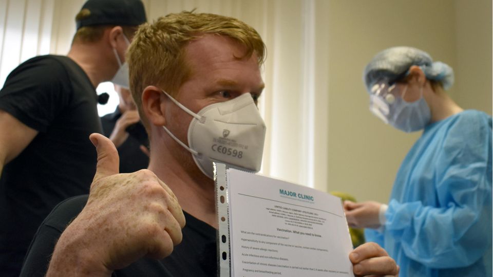 Enno Lenze hält nach der Corona-Impfung mit dem russischen Imfpstoff Sputnik V ein Blatt Papier mit Verhaltensregeln in der Hand