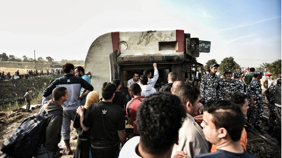 Männer und Soldaten der Streitkräfte Ägyptens stehen neben einem umgekippten Waggon eines Zugs