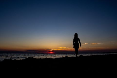 Eine Frau steht bei Sonnenuntergang am Strand