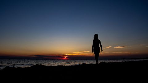 Eine Frau steht bei Sonnenuntergang am Strand