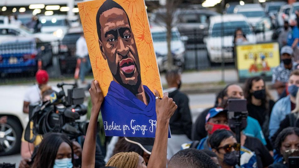 Eine Frau hebt ein gemaltes Bild von George Floyd hoch