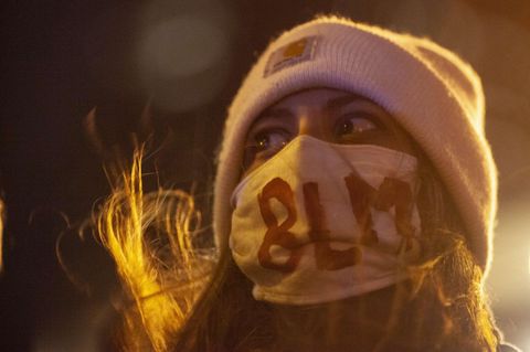 Eine Frau mit rosa Wollmütze trägt im Licht einer Straßenlaterne einen Mundschutz mit aufgemaltem "BLM"