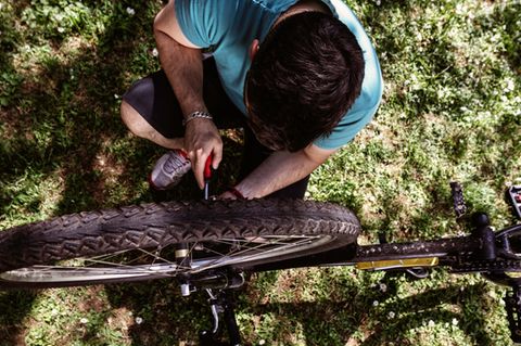 Fahrrad-Werkzeug: Junger Mann kniet mit Werkzeug neben seinem Mountainbike
