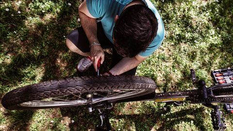 Fahrrad-Werkzeug: Junger Mann kniet mit Werkzeug neben seinem Mountainbike
