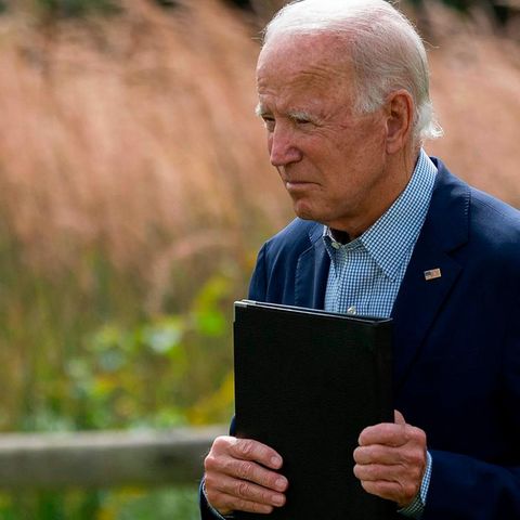 Joe Biden mit einer Kladde in der Hand vor einem Kornfeld