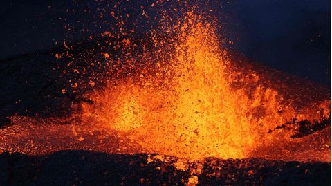 Im Dunkeln fliegt ein Schwall Lava aus einem Vulkankrater