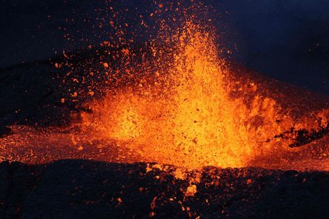 Im Dunkeln fliegt ein Schwall Lava aus einem Vulkankrater