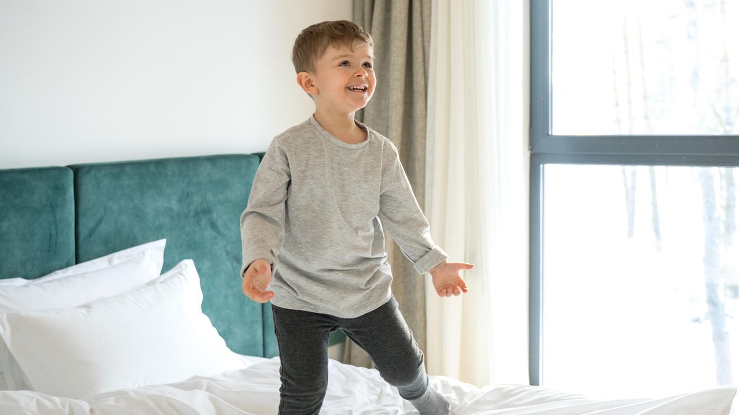 Ein kleiner Junge steht gut gelaunt im Bett und ruft etwas