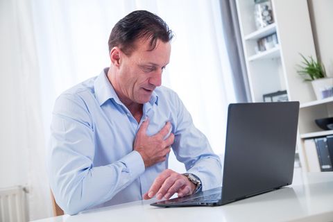 Ein Mann sitzt am Laptop und greift sich an die Brust