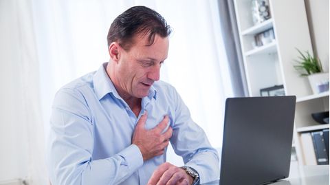 Ein Mann sitzt am Laptop und greift sich an die Brust