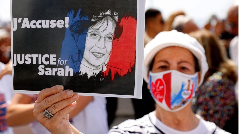 Eine Frau mit Mund-Nasen-Schutz in den französischen Nationalfarben hält auf einer Demo hält ein Schild mit Forderungen hoch