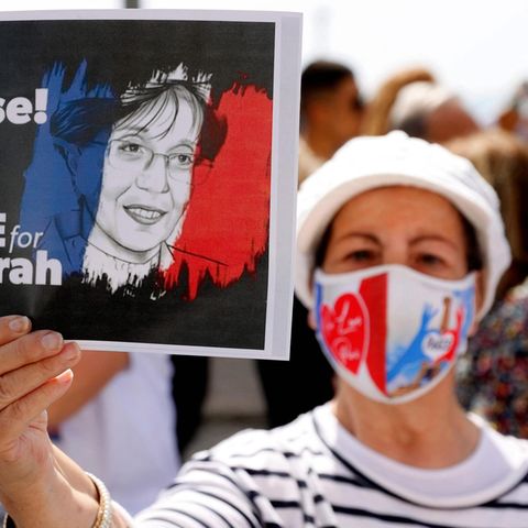 Eine Frau mit Mund-Nasen-Schutz in den französischen Nationalfarben hält auf einer Demo hält ein Schild mit Forderungen hoch