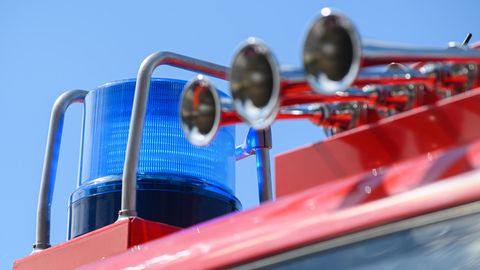 Vor blauem Himmel ist ein Blaulicht auf einem roten Feuerwehrfahrzeug zu sehen. Daneben drei chromglänzende Signalhörner